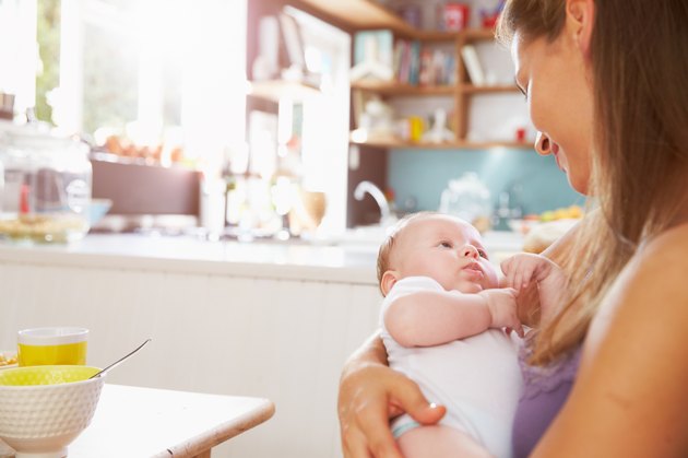Mother Holding Newborn Baby Daughter At Kitchen Table