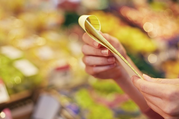 Germany, Cologne, Human hand holding shopping list in supermarket