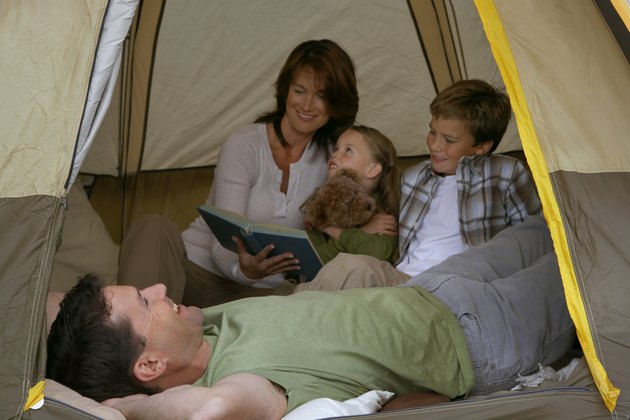 Girl (5-7 years) and boy (9-11 years) in tent with parents, mother reading story