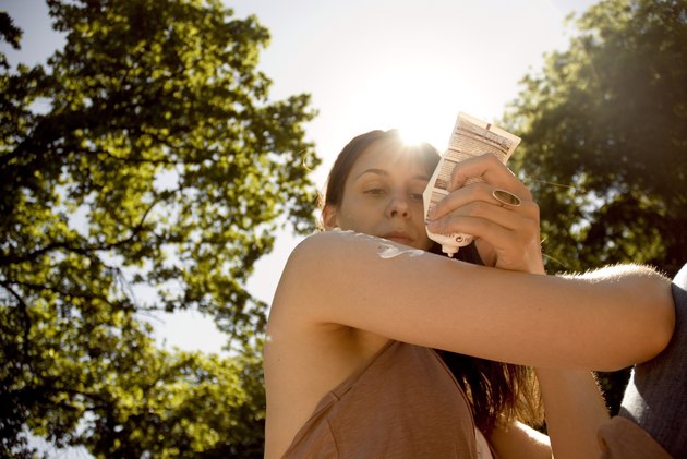 Woman applying sun cream to upper arm, low angle view (sun flare)