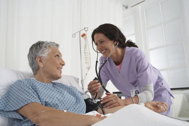 Nurse taking patients blood pressure in hospital bed, smiling