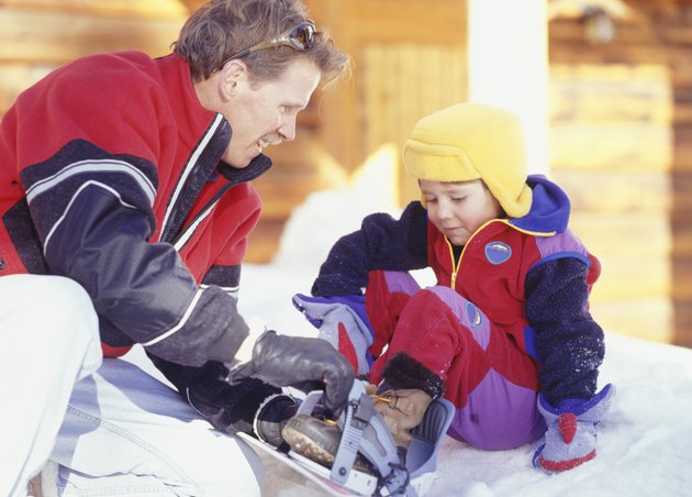Man helping son (4-5) with snowboard