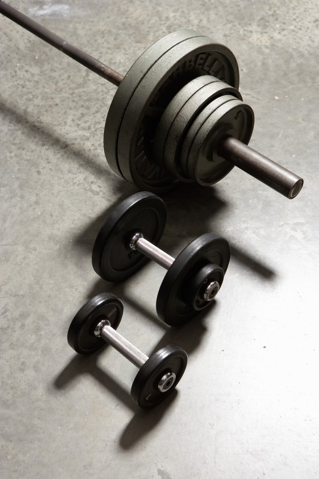 Two dumbbells and barbell side by side on concrete floor