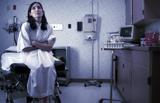a caucasian female patient in a hospital gown sits in an exam room and waits