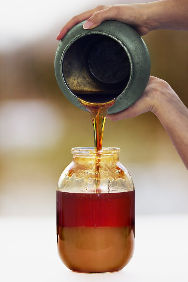 Woman's hands pours a honey from pot to a jar
