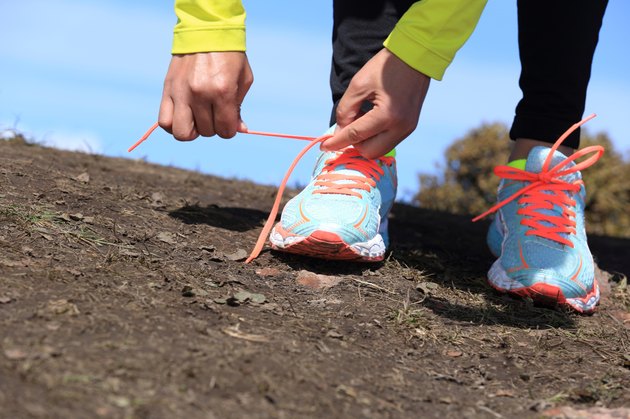young woman trail runner tying shoelace on mountain peak