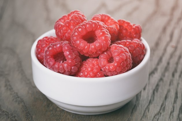 raspberries in white bowl on wood table