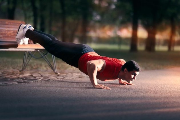 Athletic guy doing push-ups with his fit on a bench