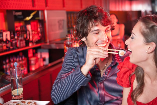 Man feeding woman sushi in nightclub and smiling