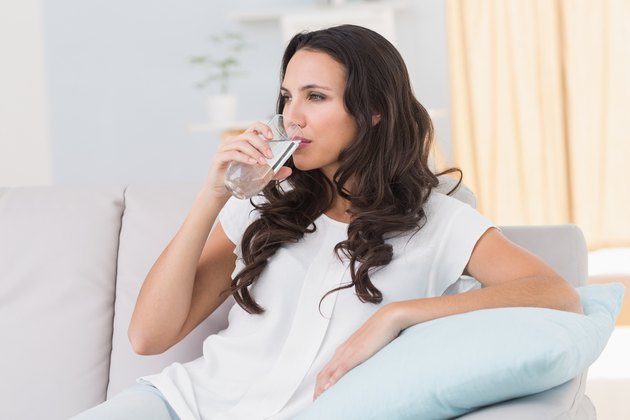 Pretty brunette drinking water on couch