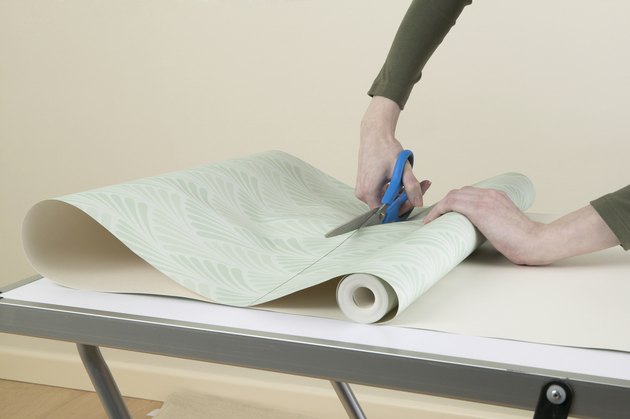 Person cutting through roll of wallpaper