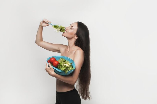 Beautiful young brunette woman with slim body holding bowl with fruits and vegetables. Healthy eating lifestyle and weight loss concept. White background