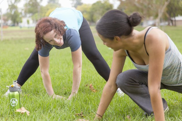 Young women wearing sports clothing on grass face to face bending over stretching