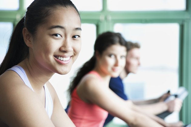 Young women exercising on fitness bikes in the gym, looking at camera