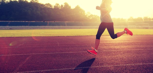 Young woman running during sunny morning on stadium track