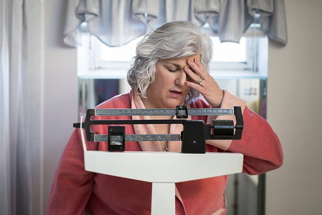 Unhappy mature woman on bathroom weighing scales