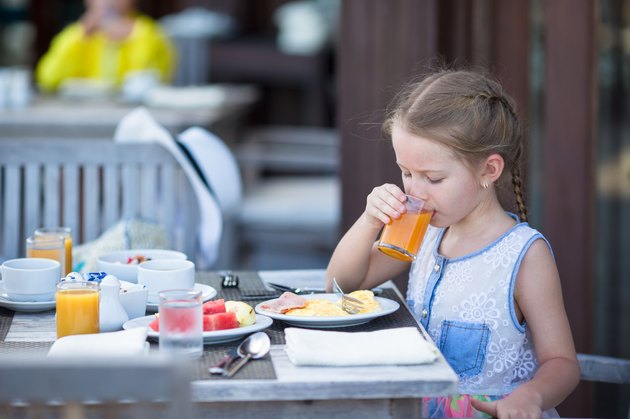 Adorable girl drinking apple juice for breakfast in outdoor cafe