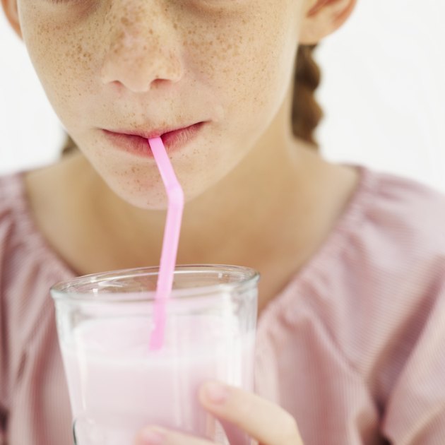 Close-up of a young girl (10-11) drinking milkshake from a glass with a straw