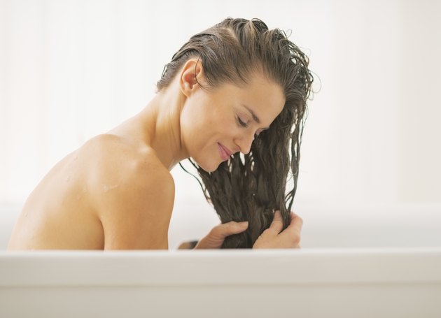 happy young woman washing hair in bathtub