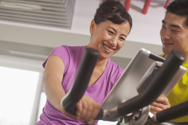 Woman smiling and exercising on the exercise bike with her trainer