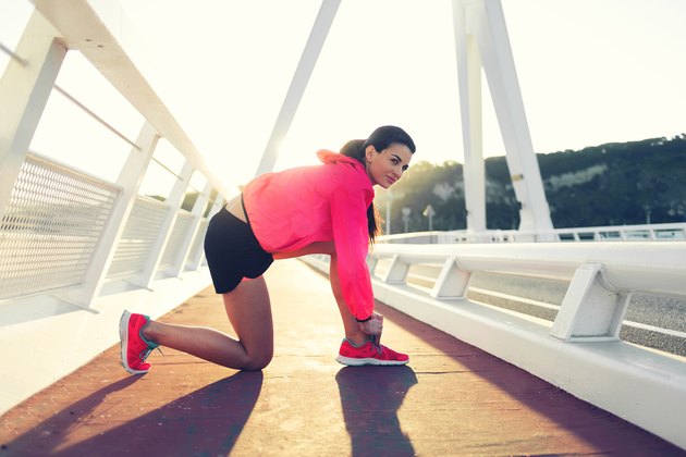 Portrait of a young female jogger dressed in sportswear tie shoelaces while taking break between evening run outside,