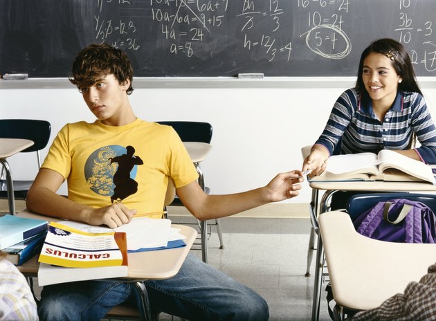 Bored Looking Boy in a Classroom Passing a Note Behind him to a Female Student