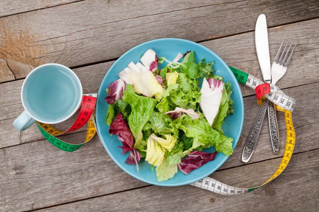 Plate with fresh salad, measure tape, cup, knife and fork