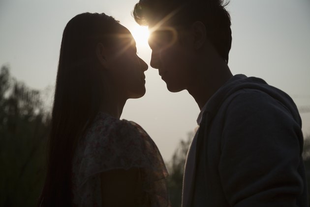 Silhouette of young couple very close to each other, sunbeam and lens flare