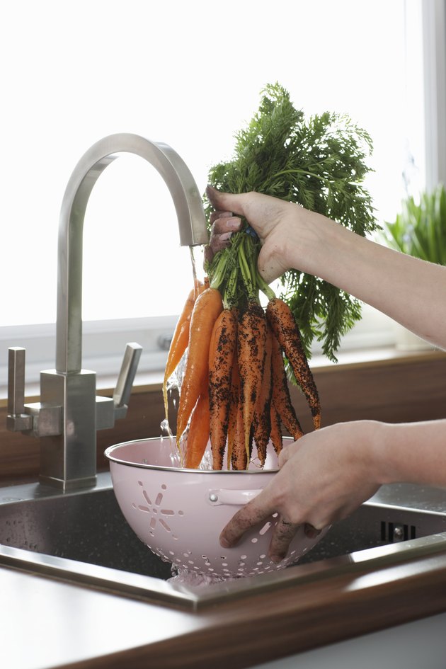Woman washing carrots at kitchen sink, close-up of hands