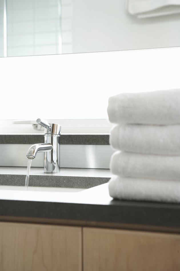 Stack of towels beside sink in bathroom, water running from faucet