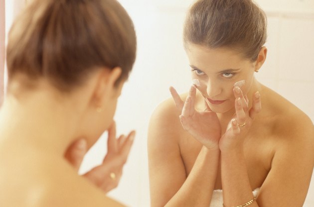 Young woman in front of bathroom mirror applying cream, rear view