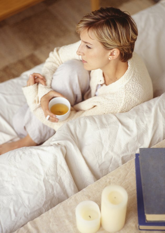 Young woman sitting drinking tea on sofa in living room, elevated view