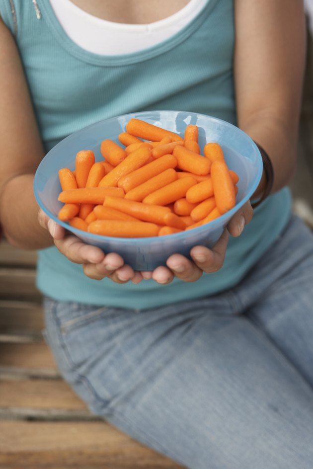 Girl (13-15) holding bowl of peeled baby carrots, close-up