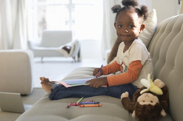 Girl (2-4) on sofa, holding crayon and paper, smiling, portrait