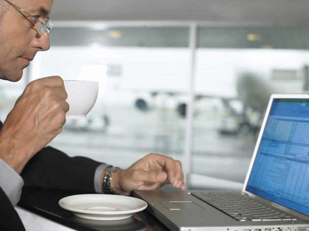 Businessman using laptop whilst drinking from cup, profile, close-up