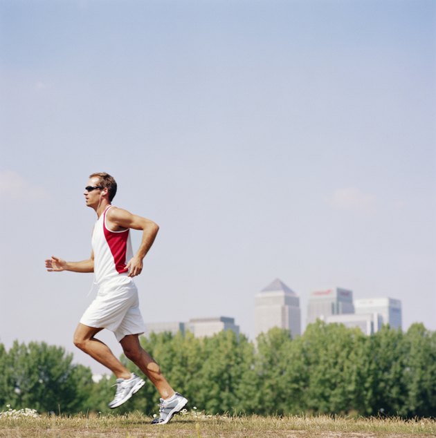 Man wearing sunglasses running in field, side view