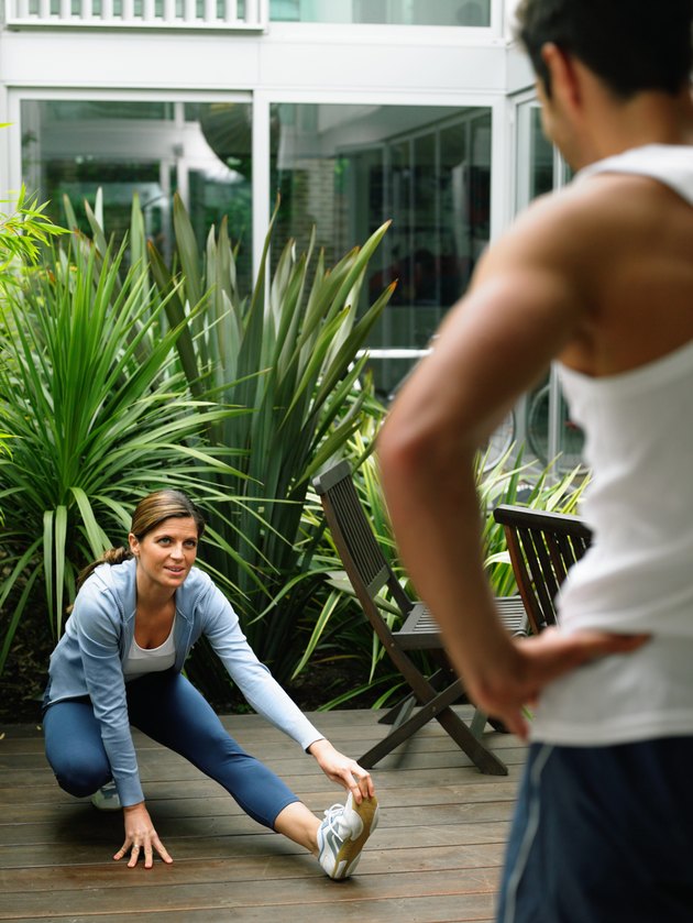Woman performing leg stretch in garden, man standing in foreground