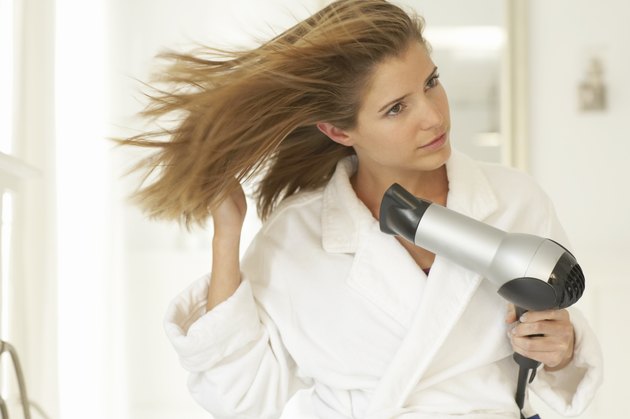 Young woman blowdrying hair, wearing dressing gown