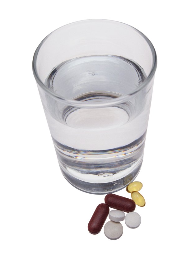 Pills and gelatin capsules beside glass of water