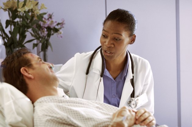 an african american doctor consults with a male caucasian patient as he lies in a hospital bed