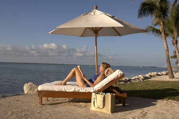 Mature woman reclining on sun lounger holding book, eyes closed