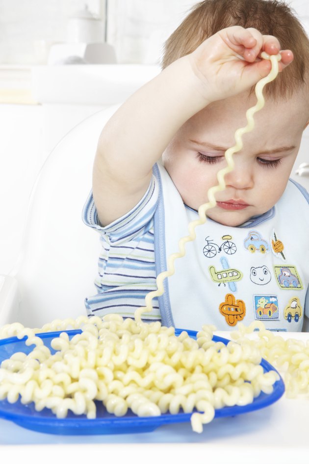 Baby boy (9-12 months) playing with pasta in high chair, close-up