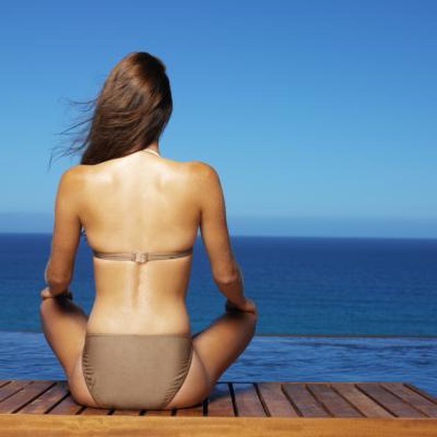 Rear view of young woman sitting on deck chair in front of ocean.