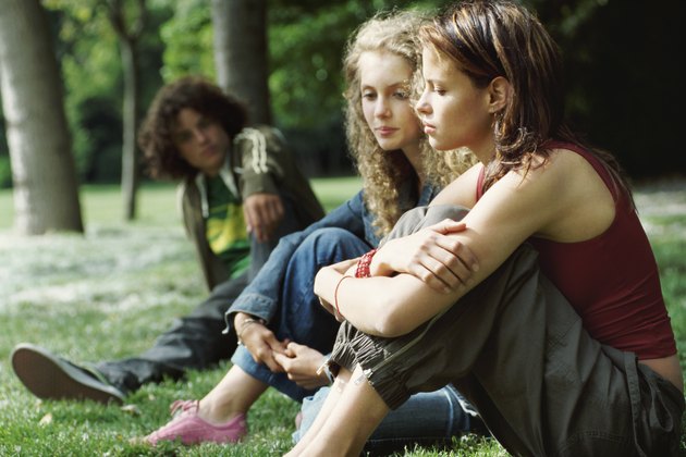 Two Young Girls Sitting on the Grass and Ignoring a Young Boy Watching Them