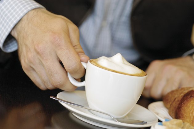 Man holding cup of cappuccino, with croissant on table