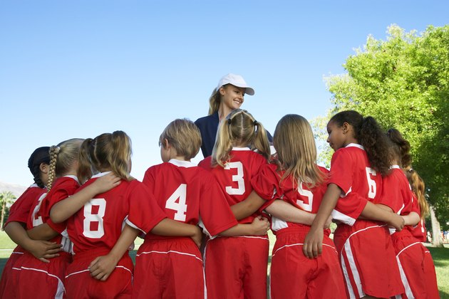 Group of children soccer players embracing standing in front of coach, back view