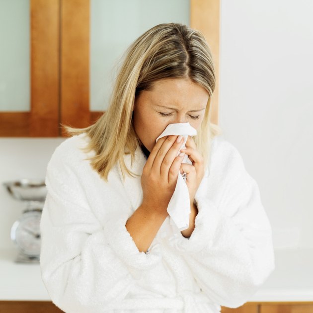 young woman in a bathrobe sneezing into a tissue
