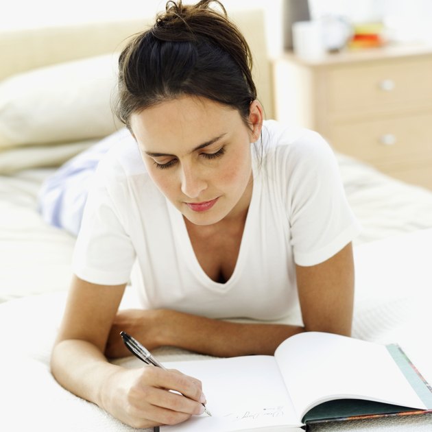 close-up of a young woman lying on the bed writing in a notebook