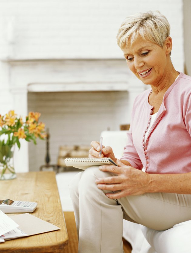 Senior woman sitting on sofa writing on notebook