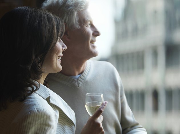 Mature couple by window, woman holding glass of wine, smiling